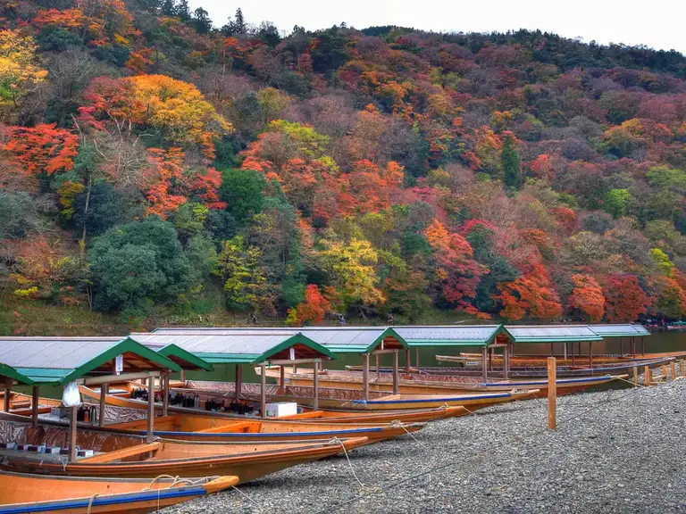Katsura river boats with autumn colors in the hills behind Arashiyama