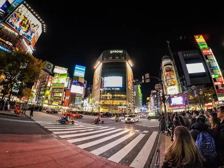 Mario Karts zip by a red light Shibuya crossing at night Shibuya